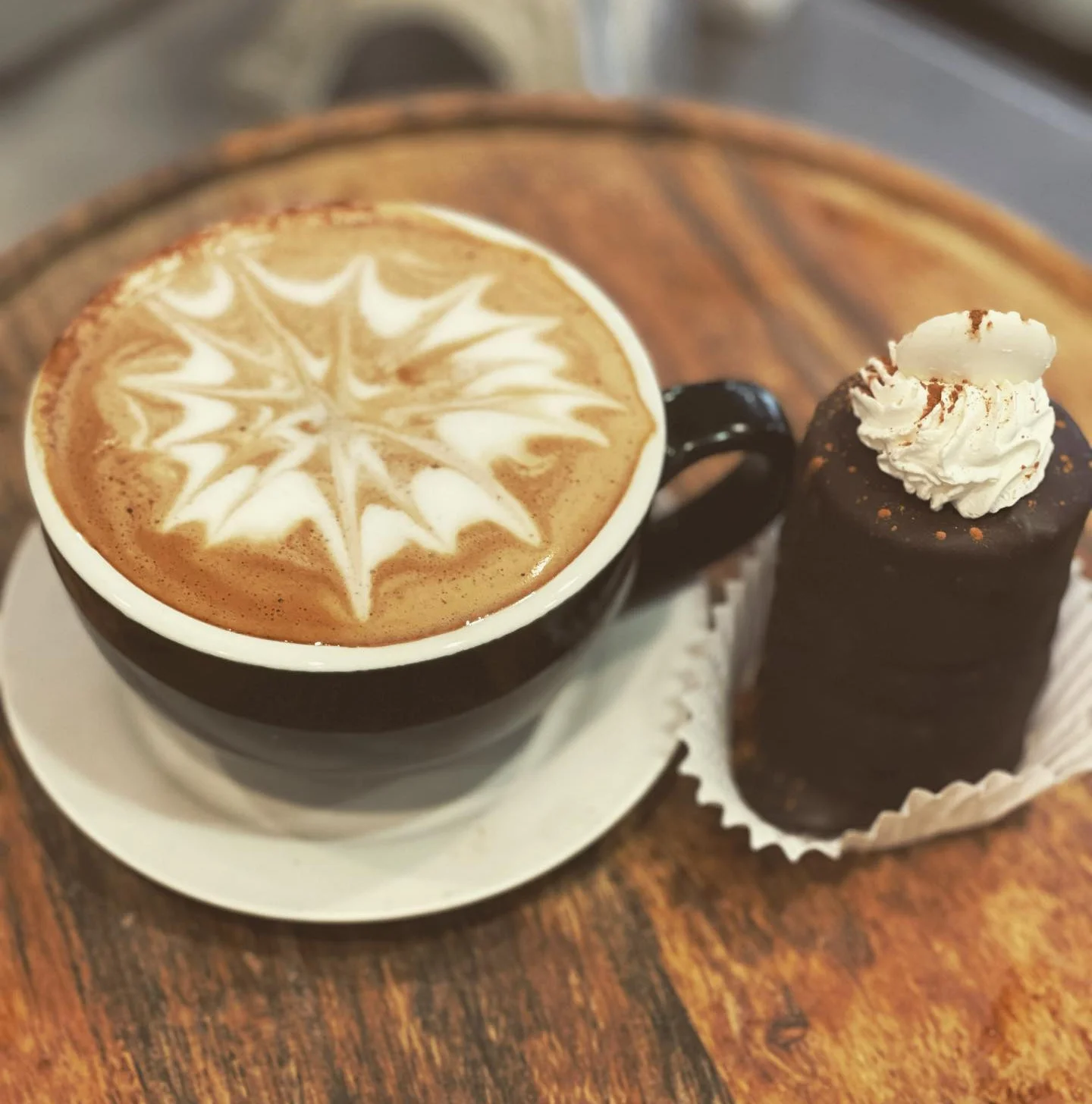 Latte with rosette art beside a chocolate pastry