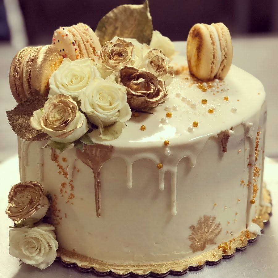 A white and gold custom celebration cake with roses and macarons